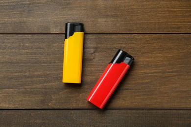 Yellow and red plastic cigarette lighters on wooden table, flat lay