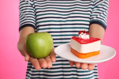 Photo of Concept of choice. Woman holding apple and cake on pink background, closeup