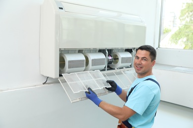 Male technician cleaning air conditioner indoors