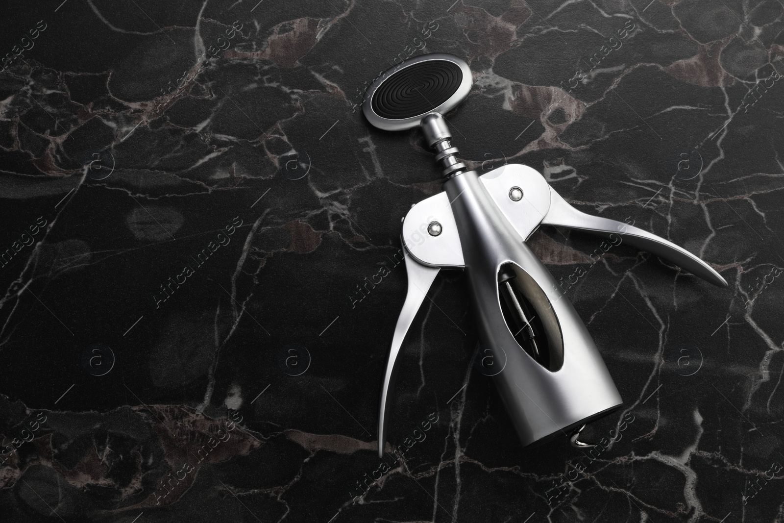 Photo of One wing corkscrew on black marble table, top view. Space for text