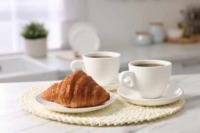 Photo of Breakfast served in kitchen. Cups of coffee and fresh croissant on white marble table