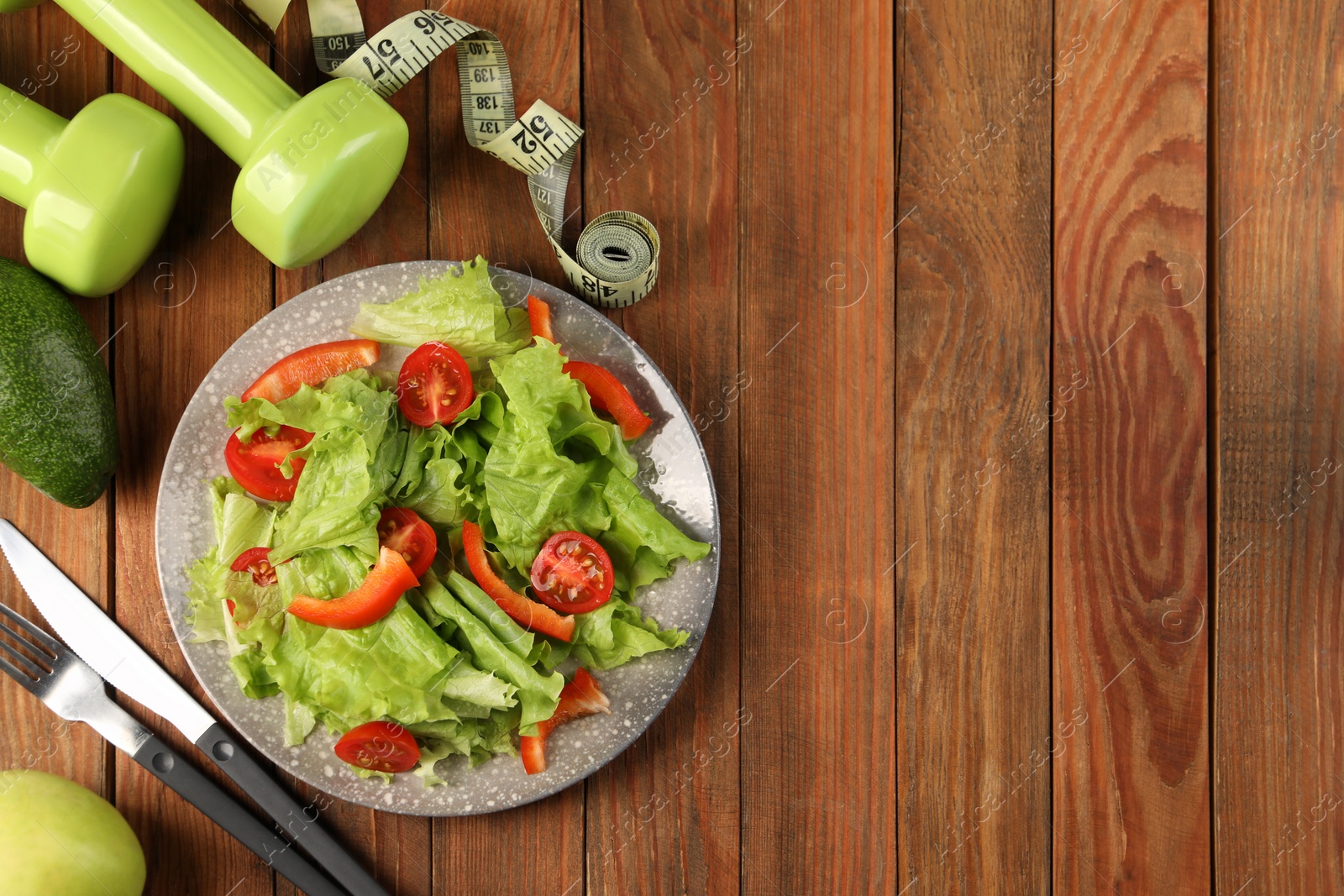 Photo of Healthy diet. Salad, cutlery, dumbbells and measuring tape on wooden table, flat lay with space for text