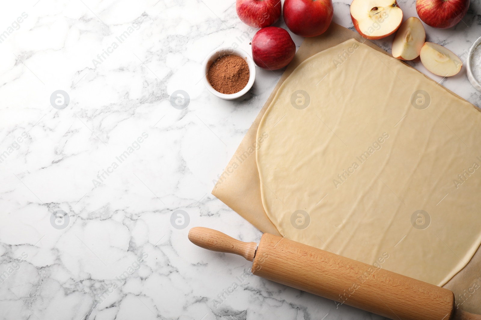 Photo of Fresh dough, rolling pin and ingredients on white marble table, flat lay and space for text. Making apple pie