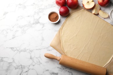 Photo of Fresh dough, rolling pin and ingredients on white marble table, flat lay and space for text. Making apple pie