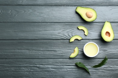 Photo of Bowl of natural oil and avocados on grey wooden background, flat lay. Space for text