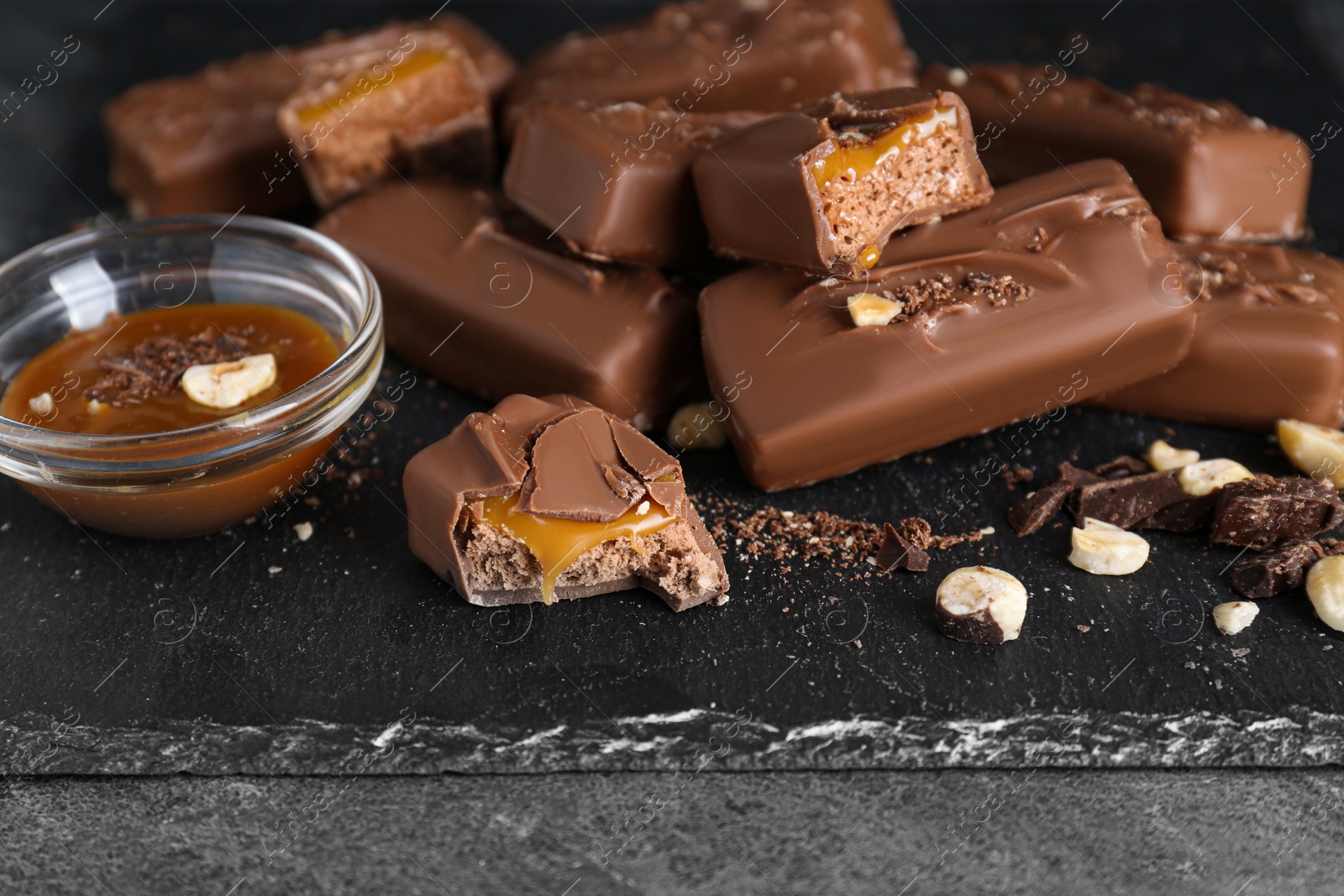 Photo of Delicious chocolate candy bars with caramel and nuts on grey table, closeup