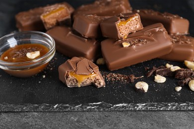 Delicious chocolate candy bars with caramel and nuts on grey table, closeup