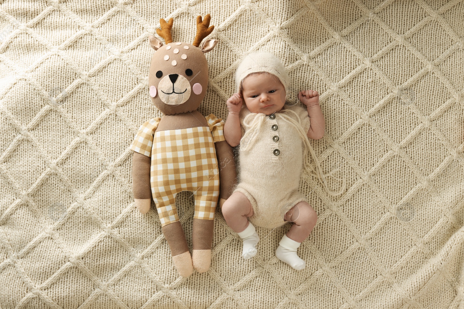 Photo of Adorable little baby with deer toy lying on blanket, top view