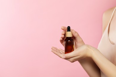 Photo of Young woman with bottle of essential oil on pink background, closeup. Space for text