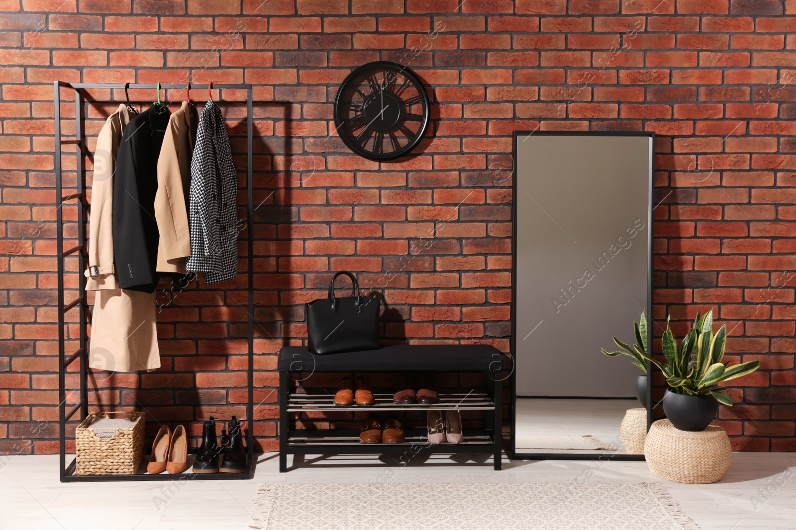 Photo of Stylish hallway with coat rack, mirror and shoe storage bench near brick wall. Interior design