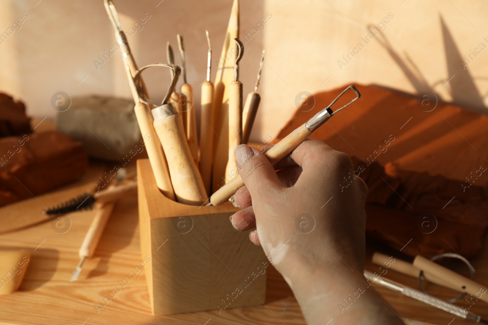 Photo of Woman taking clay crafting tool from wooden holder in workshop, closeup