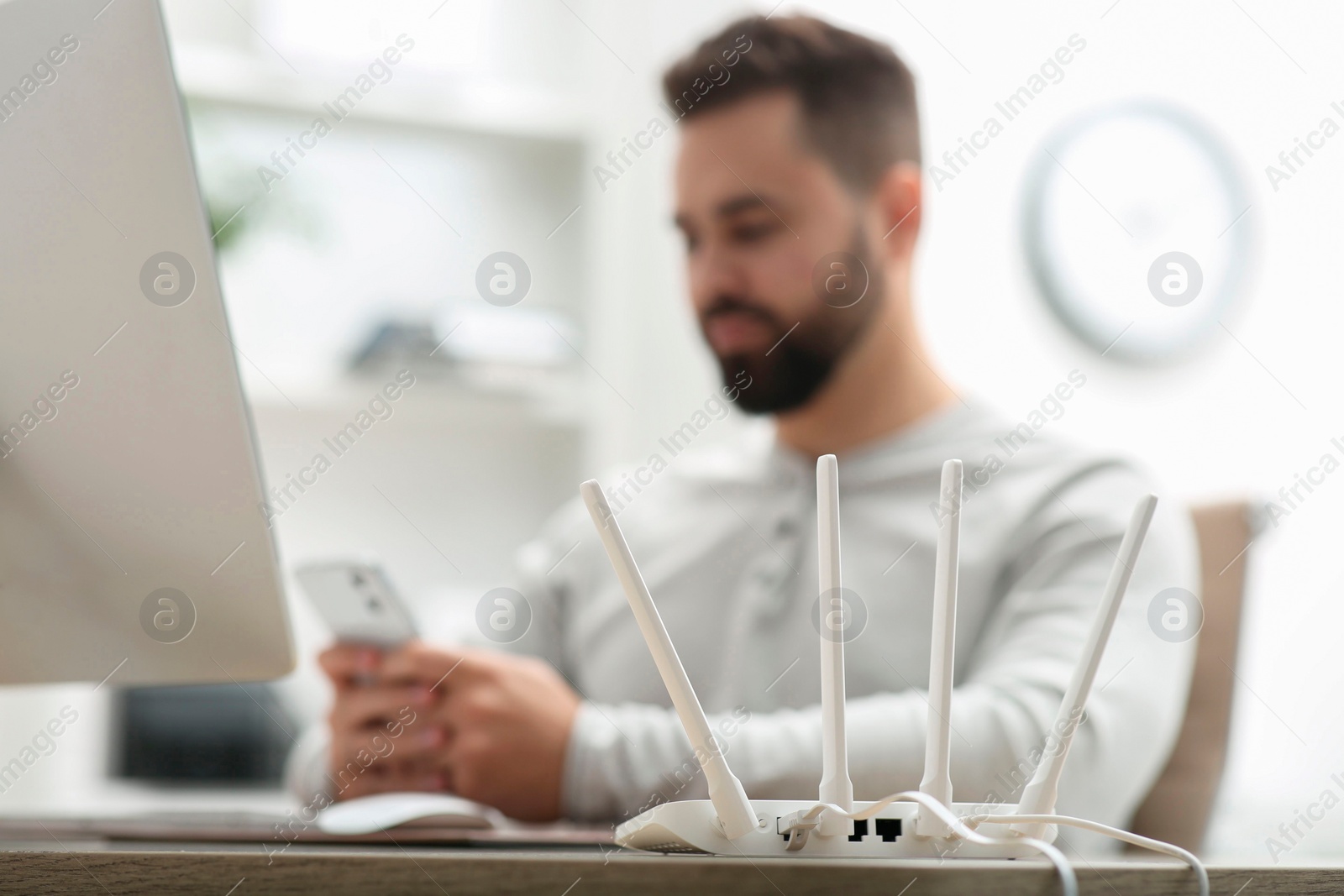 Photo of Man with smartphone working at wooden table indoors, focus on Wi-Fi router