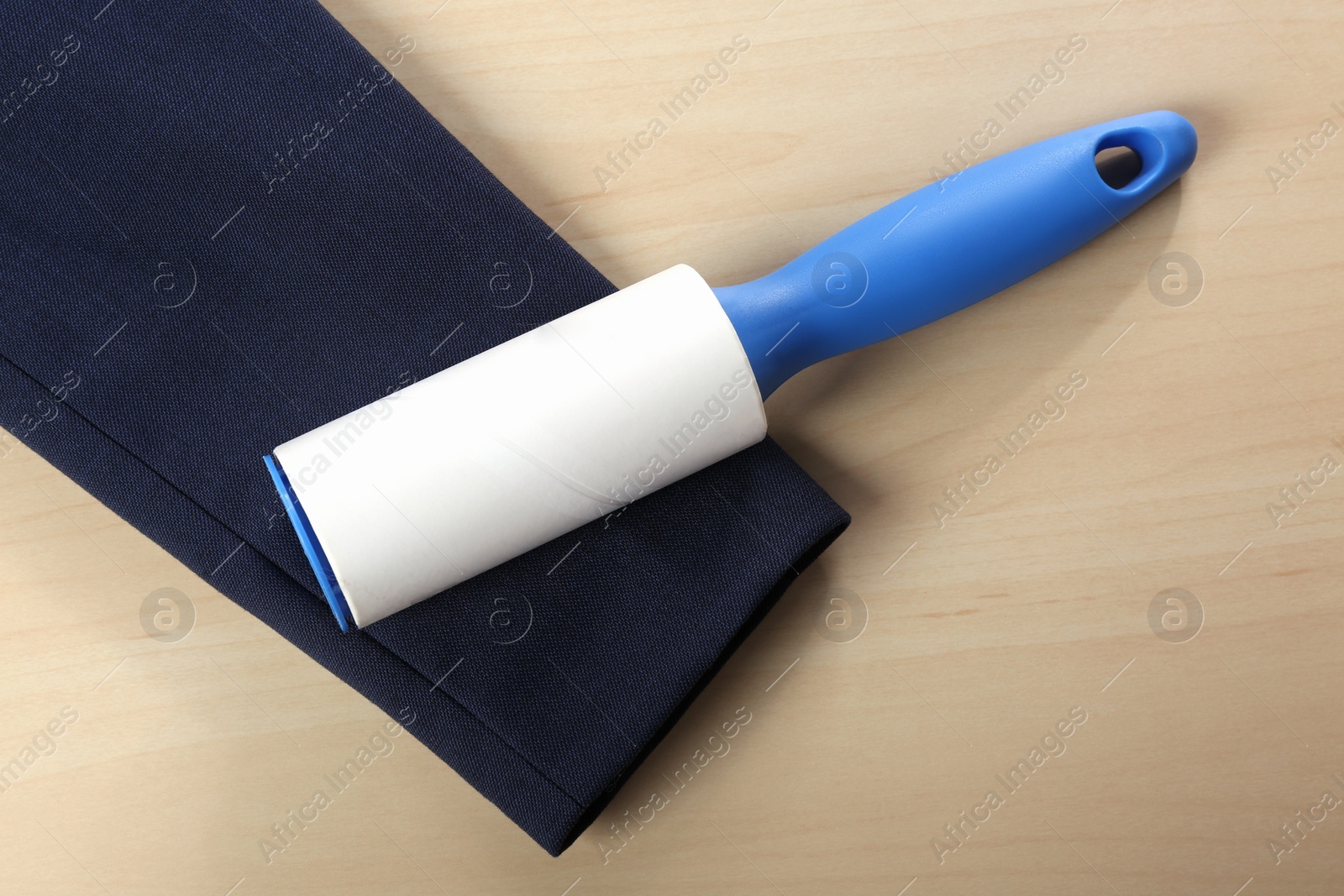 Photo of Lint roller and sleeve of jacket on wooden table, flat lay