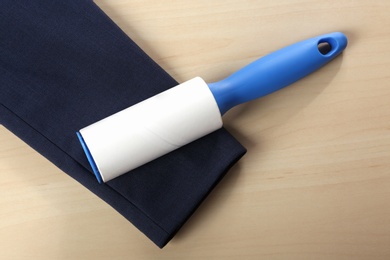 Photo of Lint roller and sleeve of jacket on wooden table, flat lay