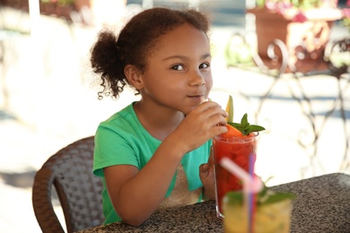 Cute African-American girl with glass of natural lemonade at table in cafe