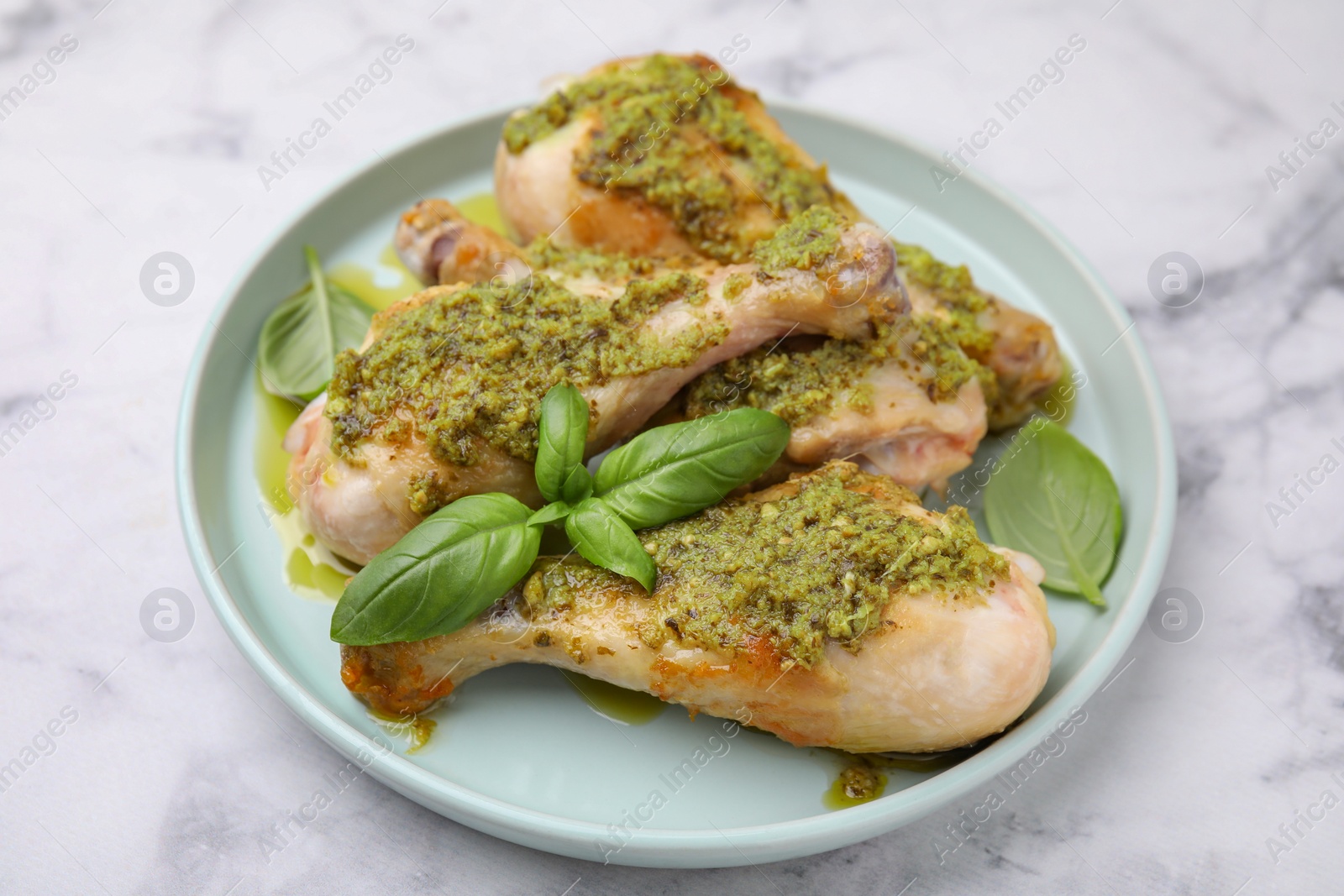 Photo of Delicious fried chicken drumsticks with pesto sauce and basil on white marble table, closeup