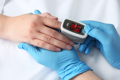 Photo of Doctor examining patient with modern fingertip pulse oximeter in bed, closeup