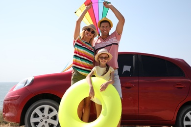 Photo of Happy family with inflatable ring and kite near car at beach