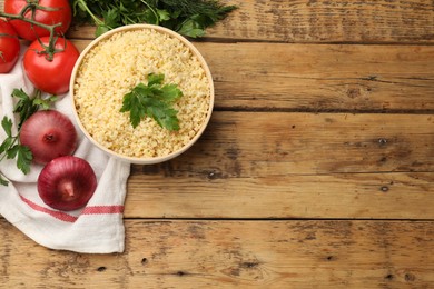 Delicious bulgur with parsley, onion, oil and tomatoes on wooden table, top view. Space for text