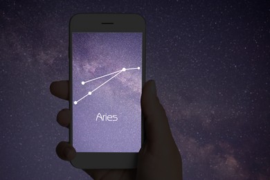 Image of Woman using stargazing app on her phone at night, closeup. Identified stick figure pattern of Aries constellation on device screen