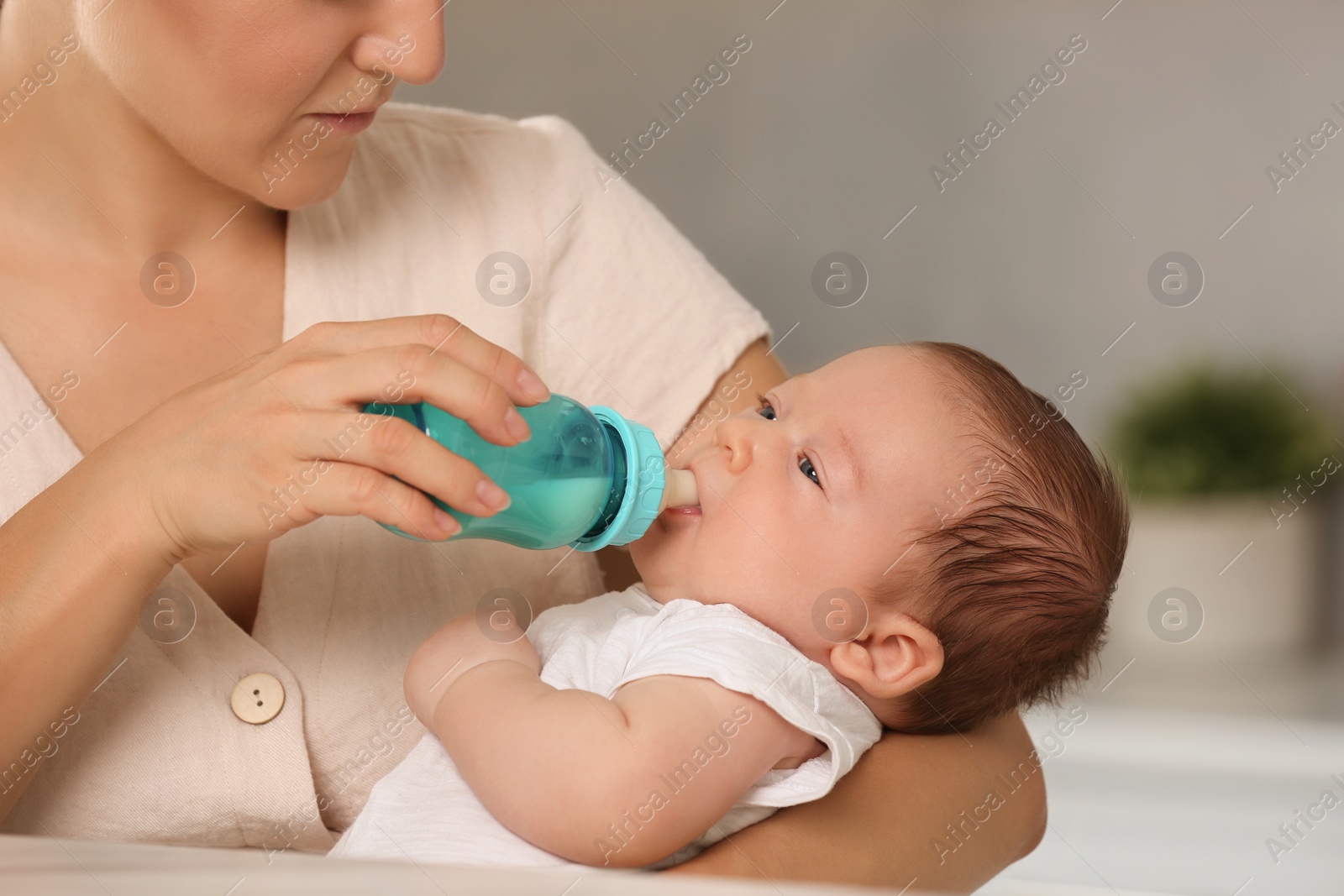 Photo of Mother feeding her cute child with infant formula indoors