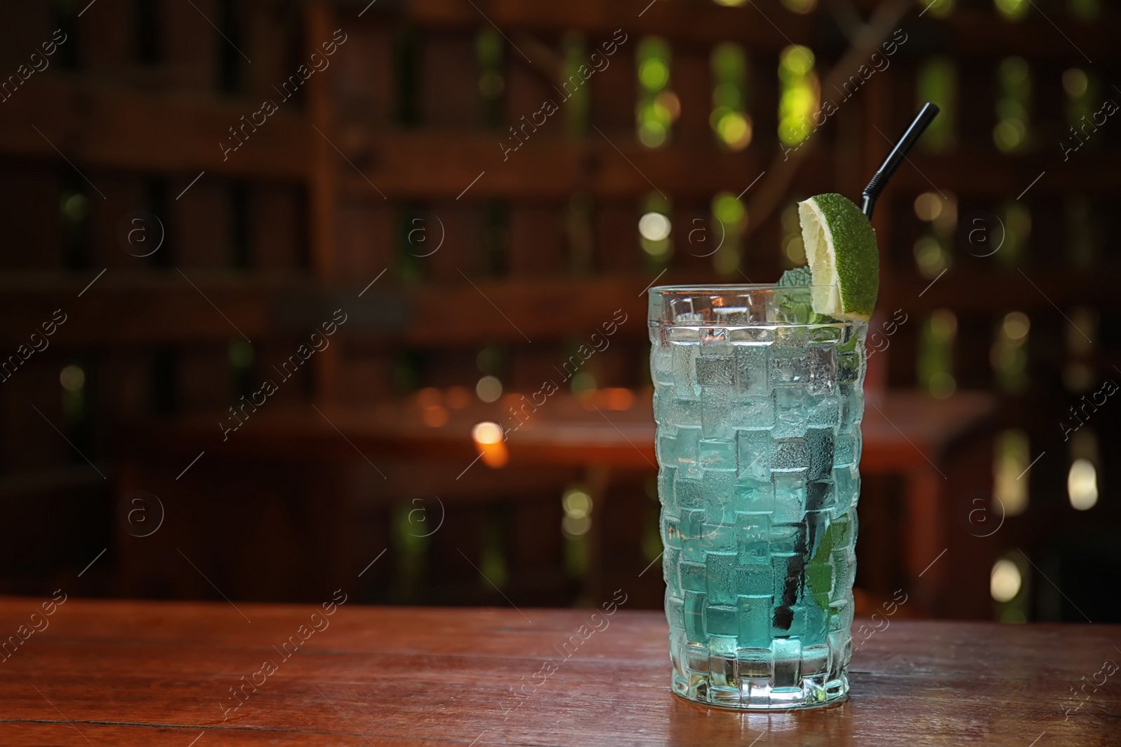 Photo of Glass with delicious cocktail and ice cubes on counter in bar