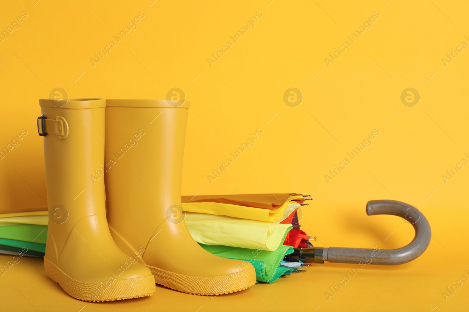 Photo of Pair of bright rubber boots near umbrella on pale orange background