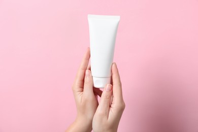 Woman with tube of hand cream on pink background, closeup