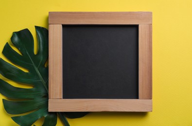 Photo of Blank chalkboard with green leaf on yellow background, flat lay. Space for text