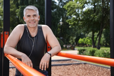 Handsome mature man having rest after exercise on sports ground, space for text. Healthy lifestyle