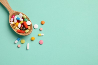 Photo of Wooden spoon with many different pills on turquoise background, flat lay. Space for text