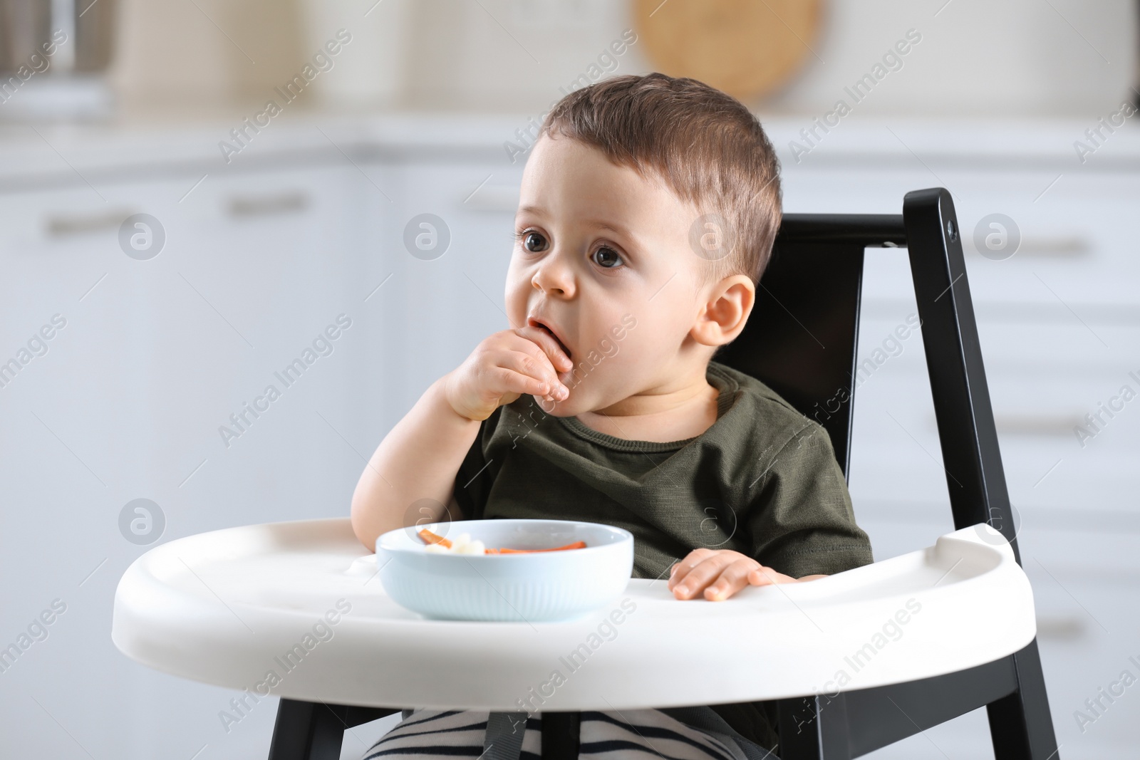 Photo of Cute little baby eating healthy food in high chair at home