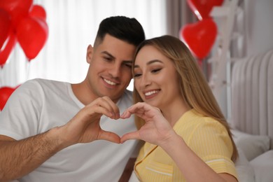 Photo of Lovely couple making heart with hands in room. Valentine's day celebration