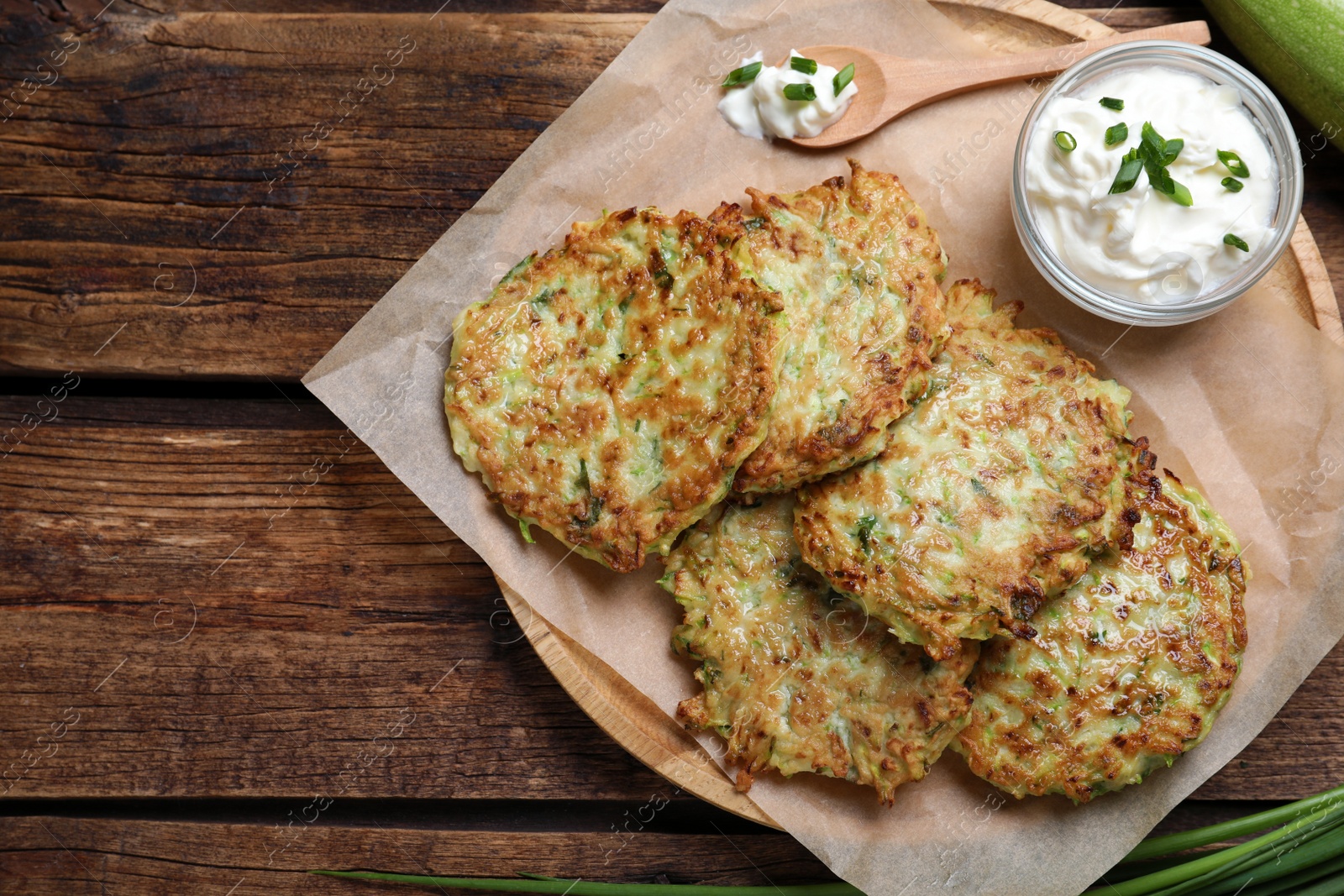Photo of Delicious zucchini fritters with sour cream served on wooden table, top view. Space for text