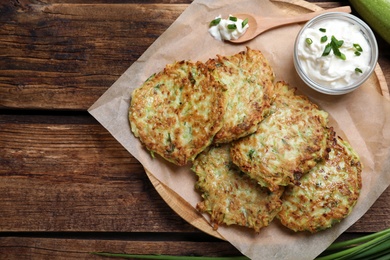 Delicious zucchini fritters with sour cream served on wooden table, top view. Space for text