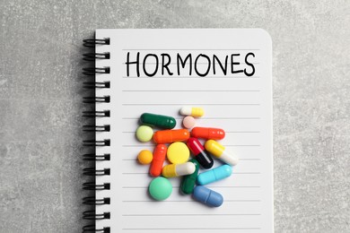 Notebook with word HORMONES and pills on grey table, top view