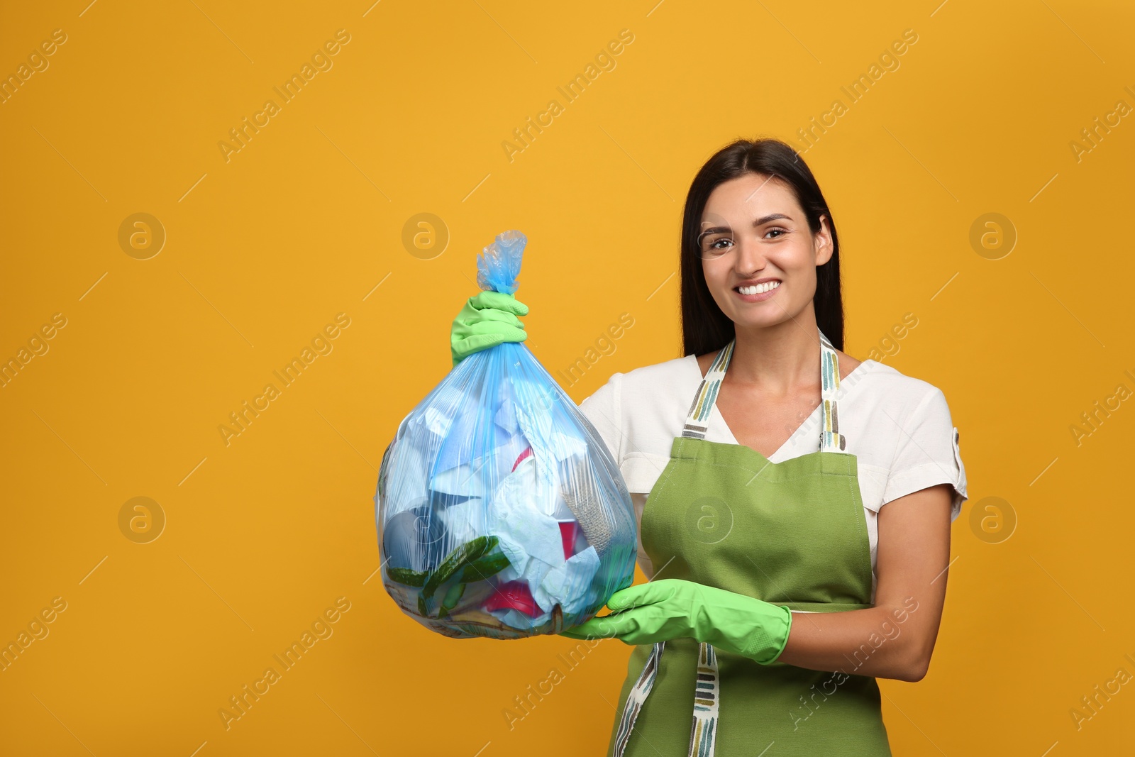 Photo of Woman holding full garbage bag on yellow background