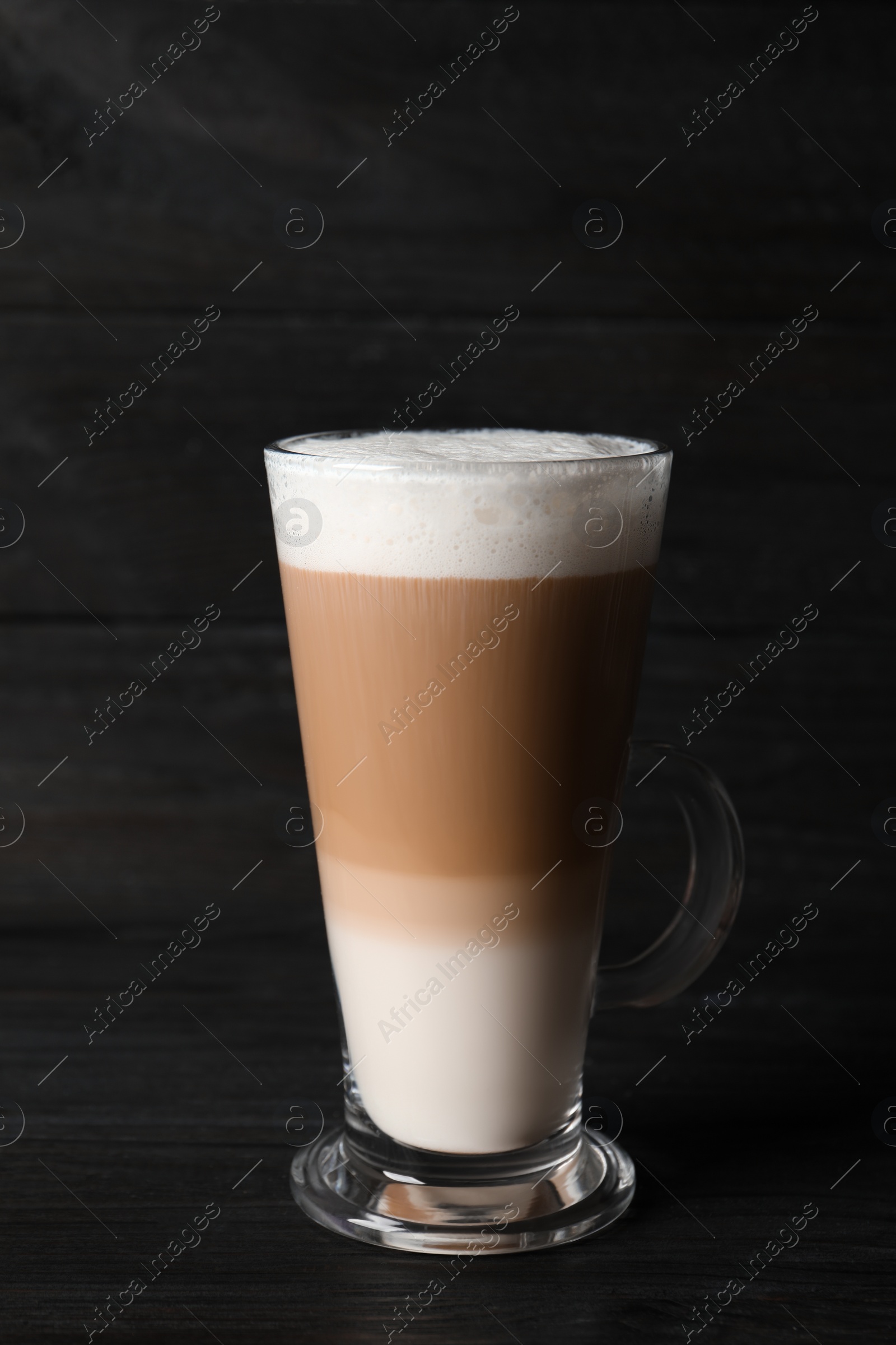 Photo of Glass cup of delicious layered coffee on black wooden table