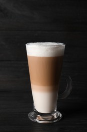 Glass cup of delicious layered coffee on black wooden table