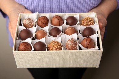 Photo of Woman holding box of delicious chocolate candies on dark background, closeup