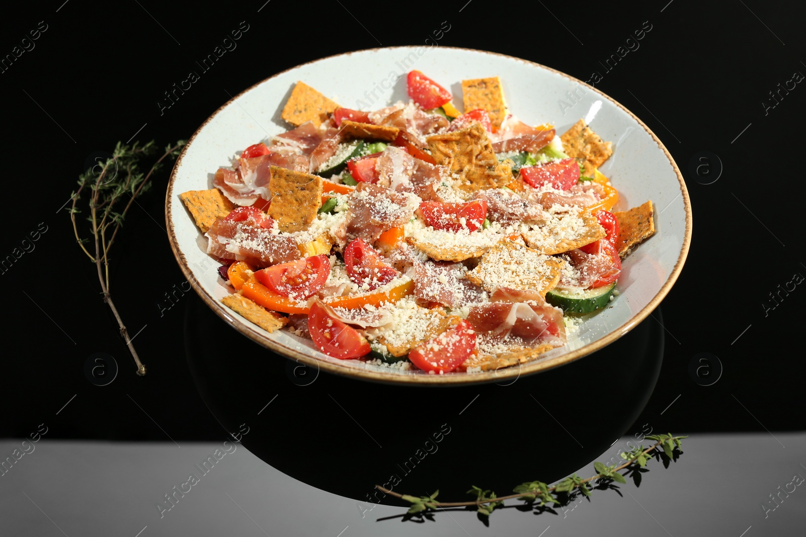 Photo of Beautiful composition of salad with prosciutto on black table in studio. Food stylist