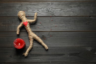 Voodoo doll, burning candle and pins on dark wooden table, flat lay. Space for text