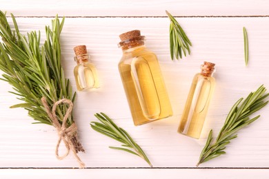 Essential oil in bottles and rosemary on white wooden table, flat lay