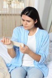 Young woman applying medical bandage onto wrist in bedroom