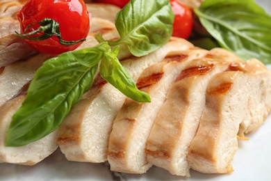 Photo of Tasty grilled chicken fillet with green basil and tomato on plate, closeup