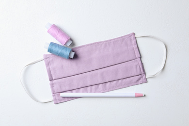 Photo of Homemade protective mask, threads and pencil on white background, flat lay. Sewing idea