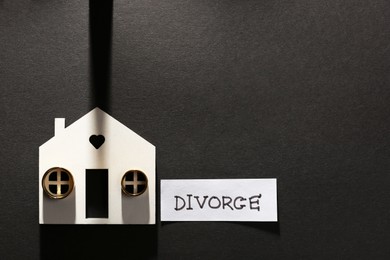 Card with word Divorce, wooden house and wedding rings on black background, flat lay. Space for text