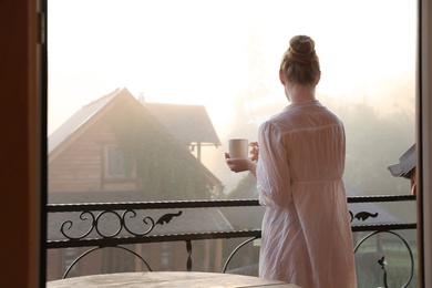 Photo of Young woman with cup of tea standing on balcony in morning