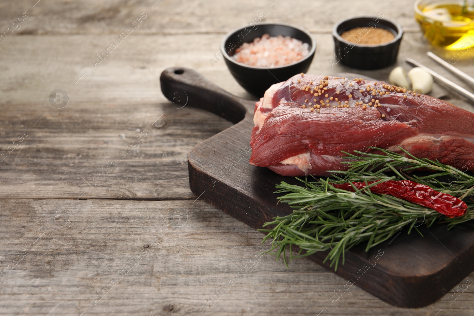 Photo of Piece of raw beef meat, rosemary, spices and chili pepper on wooden table, space for text