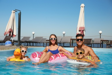 Happy family with inflatable rings in outdoor swimming pool on sunny summer day